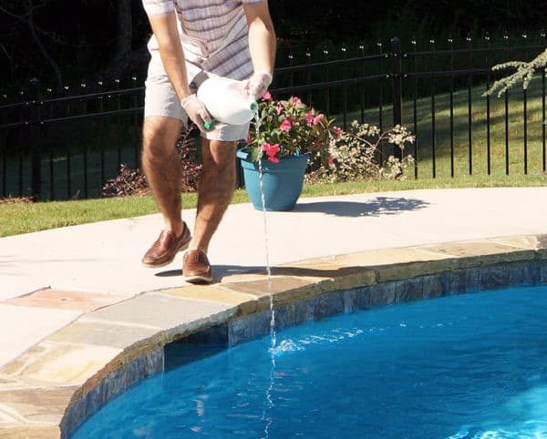 man pouring chemicals into pool
